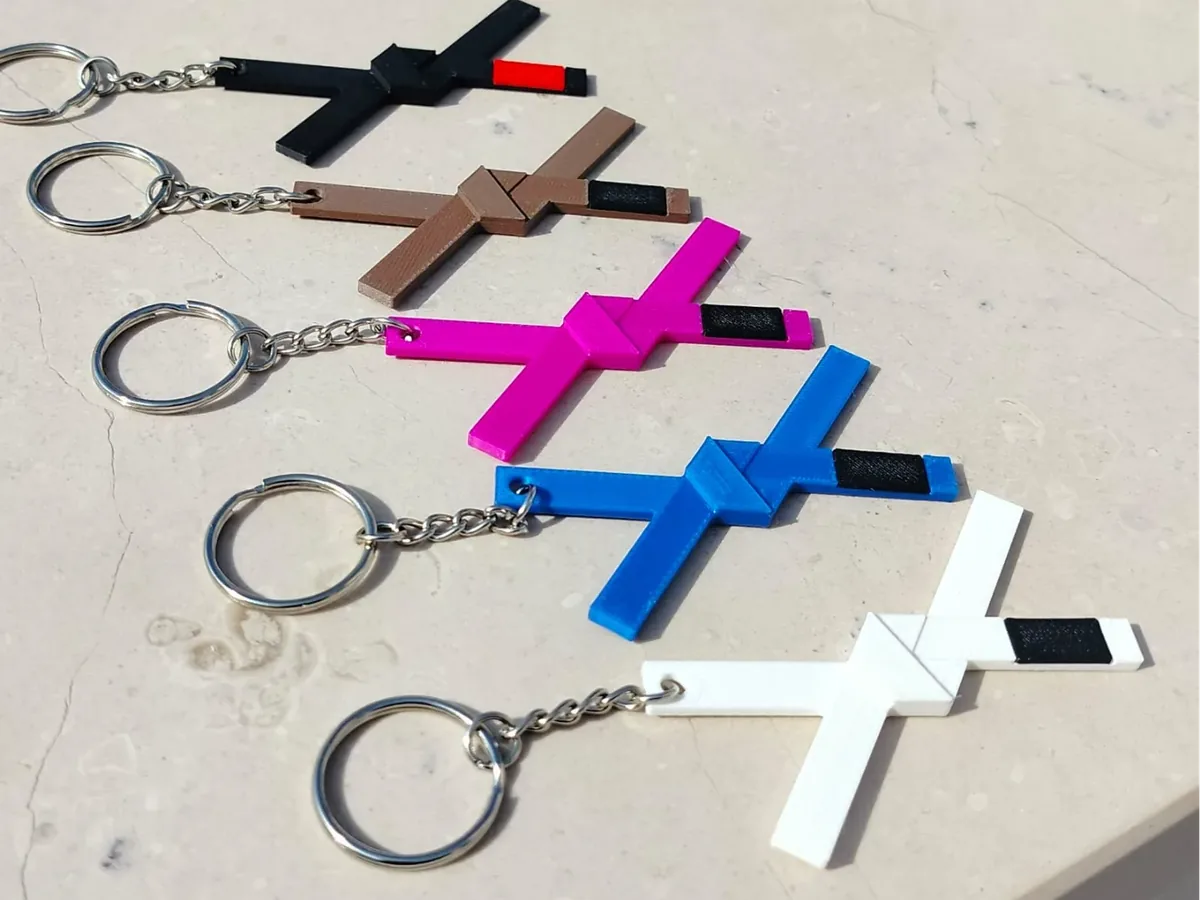 Cinco chaveiros em forma de cruz, nas cores preta, marrom, rosa, azul e branca, cada uma com uma ponteira preta.