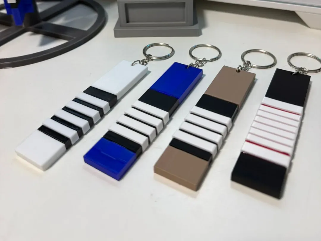 Quatro chaveiros retangulares representando faixas branca, azul, marrom e preta, com graus em relevo.