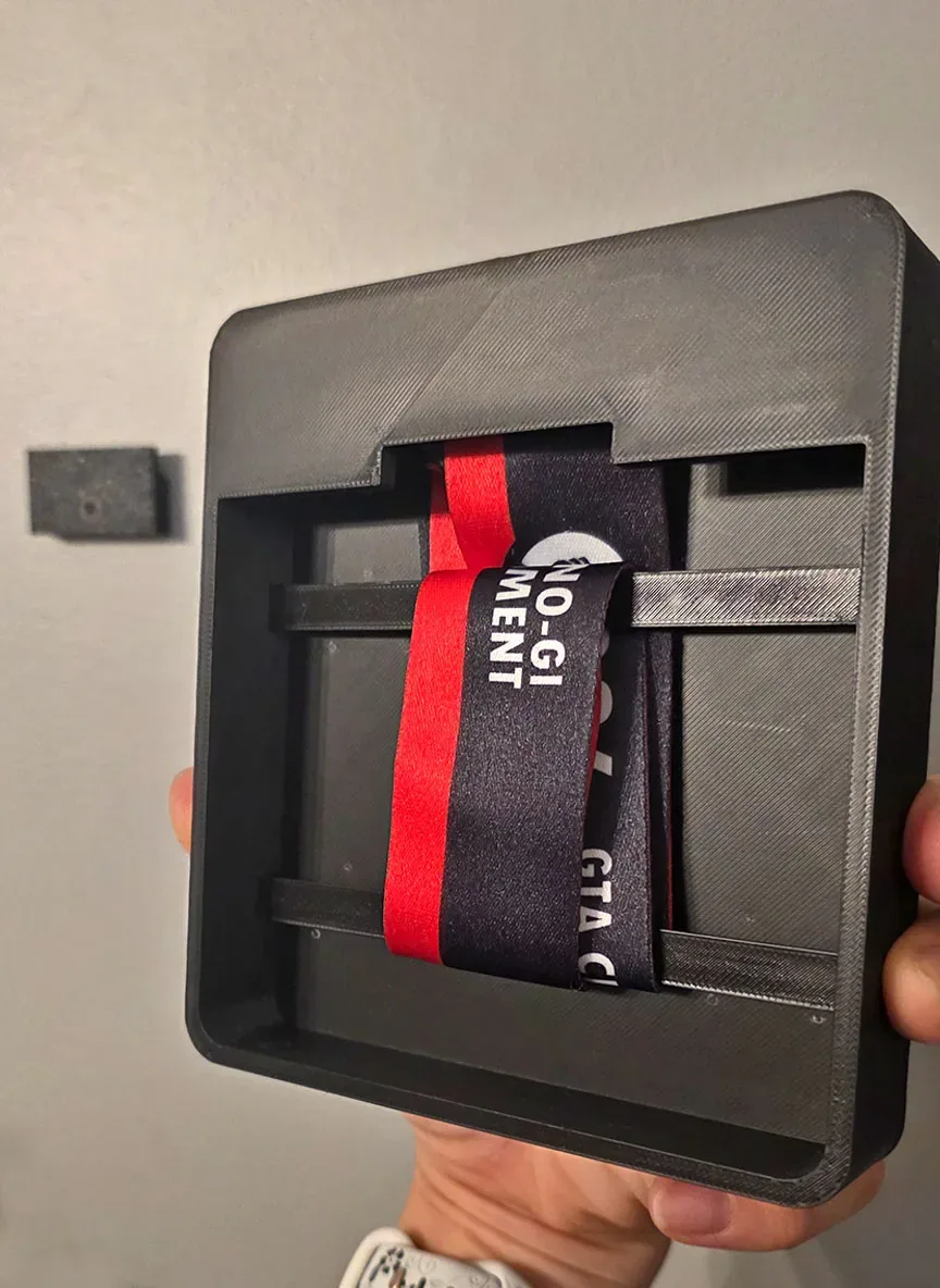 Moldura preta funda, segurada na mão, com travessas internas onde a fita da medalha passa esticada.