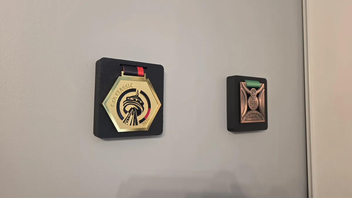 Duas placas pretas de parede, cada uma segurando uma medalha por uma fenda no topo.