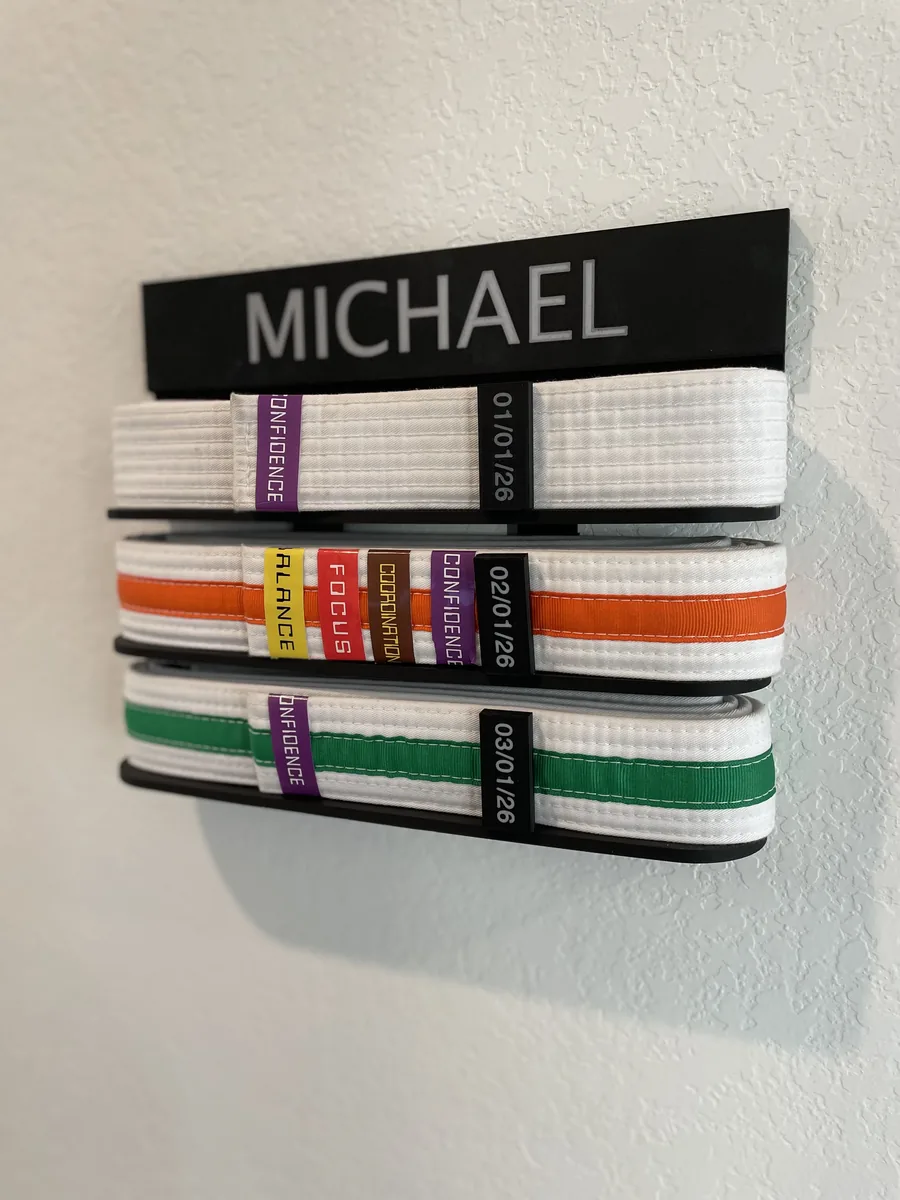 Suporte de parede preto com o nome MICHAEL no topo, segurando três faixas brancas com listras colorida, cada uma com etiquetas de data e de valores.